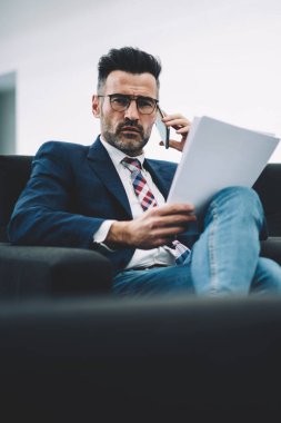 Formal giyim konuşmak smartphone telefon telefon sırasında emin olgun işadamı portresi. Deneyimli girişimci metin belgesine finansal raporlar denetlerken cep üzerinde iletişim