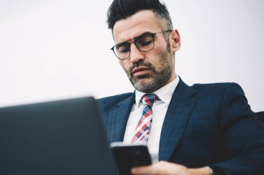 Kendine güvenen orta yaşlı işadamı gelen bildirim Smartphone cep telefonu ile 4 g internet bağlantısı üzerinden dizüstü bilgisayarda yazılım yenilemeler yaparken okuma takım elbiseli. Dalgın gurur CEO'su posta cep üzerinde kontrol