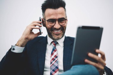 Neşeli olgun gurur CEO'su 50 yaşında dijital dokunmatik yüzey üzerinde komik bilgileri okuyun ve iş ortağı için smartphone üzerinde arama formal giyim giymiş. Cep telefonu üzerinde konuşurken mutlu Finans Müdürü