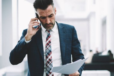Muhasebe raporlarında mali sorunları çözmek için kendine güvenen gurur CEO'su formal giyim smartphone üzerinde arama içinde. Hareket eden telefon aygıt Office İç konuşurken elinde belgelerle ciddi iş adamı