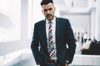 Yarım uzunluk portre başarılı emin işadamı formal giyim ayakta ofiste giyinmiş. Takım elbiseli ciddi olgun gurur CEO'su. Kameraya bakarak müreffeh orta yaşlı girişimci