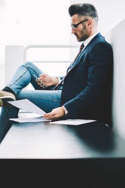 Yan görünüm deneyimli gurur CEO'su orta yaşlı smartphone aygıt üzerinde gelen bildirim bağlı 4 g için okuma Internet. Elinde telefon üstünde posta kontrol belgeleri ile dalgın işadamı