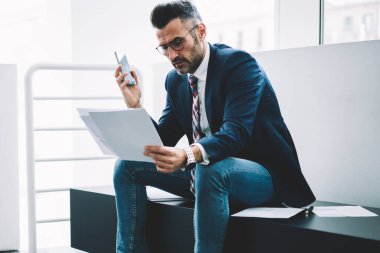 Dalgın olgun girişimci muhasebe raporları bilgi verilerle kontrol formal giyim giymiş. Ofis iç oturan deneyimli işadamı orta yaşlı okuma mali metin belgeleri