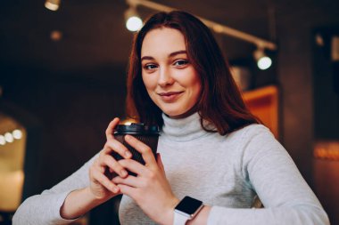 Kafeteryadaki kahve molasında dinlenen esmer kadın öğrencinin portresi, günlük giysiler içinde gülümseyen genç bir kadın blog için not defterinde makale oluşturmaya başladığı için aroma içeceğinin tadını çıkarıyor.