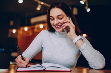 Telefon görüşmesi tamamlanmış kurs hakkında good news paylaşmak için genç hippi kız gülümseyerek, ödev yazma ve Smartphone'da arkadaşla konuşurken mutlu genç kadını tatmin ile tarifeleri