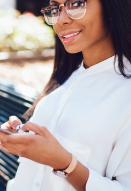 Koyu tenli kameraya smartphone aygıt yolu ile şehir merkezindeki bankta oturmuş 4 g internet bağlantısı üzerinde online sohbet mesajlaşma süre gülümseyen başarılı çekici genç kadın portresi kırpılmış