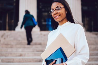 Yarım uzunlukta klasör ve dokunmatik yüzey fotoğraf makinesi ayakta Üniversitesi karşı gülümseyen elinde tutan Hukuk Fakültesi başarılı Afro-Amerikan öğrenci portresi. Zengin kadın ofis çalışanı