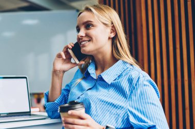 Kahve fincanı, kadın işçilerin çalışma mola sırasında telefon konuşmayı tutan mockup ekranlı dizüstü yakınındaki çalışma evinde oturan cep telefonu zekâ arkadaş konuşurken neşeli sarışın kadın