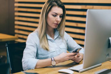E-posta kontrol ve bildirim Smartphone cep telefonu ile okuma dalgın genç kadın bağlı 4 g için internet iş yerinde modern bilgisayar sırasında. Kadın ofis çalışanı profil sayfası işyeri üzerinde oturan telefon güncelleme