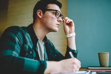 Akıllı genç hipster adam sorun çözüm coworking boşluk, notlar ve planlama kurs için yaratıcı fikir konsantre Eyewear düşünceli erkek öğrenci ödev hakkında düşünme