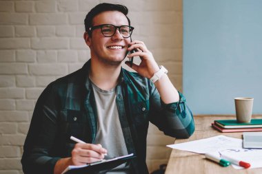 Neşeli erkek serbest meslek sahibi iyi ruh hali planlayıcısı yazma eğitimi sırasında smartphone konuşmayı kafe iç, mutlu hipster adam çalışan proje hakkında telefon paylaşım iyi haber verme