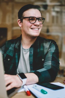 Neşeli hipster erkekte erkek öğrenci uzak yazarak geribildirim online sohbet arıyorsunuz gözlük gülümseyen serbest dizüstü bilgisayar, café iç yazarak yayın makale zevk gözlükler