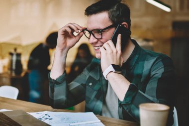 Dizüstü bilgisayar telefon görüşmesi, kafede çalışırken netbook üzerinde web sayfasına göz dostu cep telefonu konuşmayı neşeli hipster adam webinar izlerken Eyewear mutlu genç adam