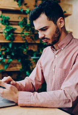 Ciddi genç erkek freelancer uzay coworking oturan smartphone posta denetlerken kötü haber ile hayal kırıklığına uğrattı, hipster adam bankacılık denge yolu ile cellphone üzerinde app okuma hakkında kızgın vurguladı