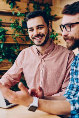Kamera işbirliği yaparken, birlikte dizüstü bilgisayar kullanan projede çalışan yetenekli erkek programcılar açıklayan bilgi ve fikir onun arkadaşı süre bakarak neşeli yakışıklı adam portresi