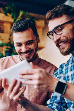Neşeli genç hipster çocuklar, birlikte touchpad ile sosyal ağlardan komik videolar izlemek eğlenceli sahip gülümseyen iskambil online spor üstünde taşınabilir pc arkadaş için onun sonuçlarını gösteren adam sakallı