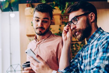 Duygusal hipster adam akıllı telefon bildirim seyir ve şok alış irsaliyesi bill, alma ile genç adam kötü getting haber cep üzerinde hayal kırıklığına duygu onun arkadaşıyla haber okuma vurguladı