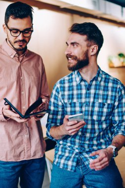 Neşeli hipster adam meslektaşı gülümseyen iletişim iş smartphone, bilgi iş arkadaşınız ile işbirliği için tartışmaya ile adam holding Not defteri kullanarak planlama hakkında ofiste bakarak