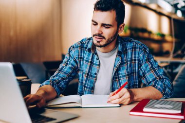 Erkek öğrenci, internetteki internet kursları vasıtasıyla öğrenim görmek için internet üzerinden bilgi topluyor. Sosyal ağlarda yayınlamak için dizüstü bilgisayar yazıları kullanan hippi çocuk.