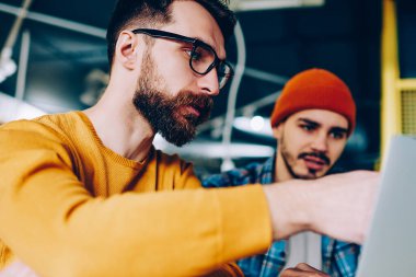 Yetenekli erkek, geliştirme eğitmeni, dizüstü bilgisayarı işaret eden eğitmen ve arkadaşlarıyla iletişim kuran hipster bir adamın internet sitesinde yeni bir uygulama göstermesi.