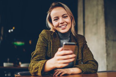 Mutlu kadın Blogger yarım uzunluk portre profil sayfası smartphone aygıt kameraya gülümseyen süre 4g internet bağlantısı ile güncelleme şık giyim giymiş. Neşeli sahibi elinde cep ile