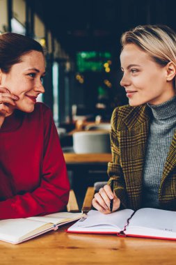 İki yaratıcı öğrenci işbirliği ile bloknot alan coworking içinde vasıl okul sırası oturan üretken strateji tartışıyor. Casual kıyafet birlikte ortak proje üzerinde çalışan kadın tasarımcılar gülümseyen