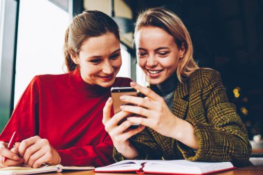 Canlı izlerken olumlu kız öğrenci blog Smartphone cep telefonu ile akışında bağlı 4 g internet kafede sınava hazırlık sırasında. Mutlu genç kadın telefonu sosyal ağlar komik yorum okuma
