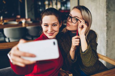Casual giyim poz ve selfie fotoğraflar yayın için modern smartphone cep telefonu ile sosyal ağlar kafede dostu toplantı sırasında iç yapım komik suratlar ile iki başarılı kadın blogcular