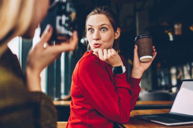 Kahve molası sırasında eğlenmek vintage fotoğraf makinesinde poz yüzündeki komik yüz buruşturma ile pozitif kadın blogger. Hippi kız odaklanan sosyal ağlarda yayın için en iyi arkadaşınızın fotoğrafını yapmak