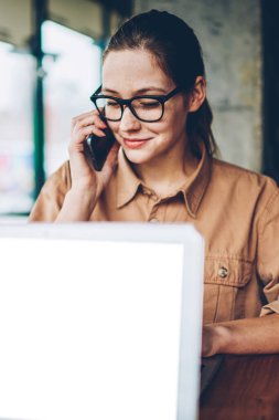 Esmer kadın Yöneticisi smartphone üzerinde arama gözlük '. Freelancer işleci ile mobil faydaları sırasında telefonla söz Eyewear dizüstü bilgisayarda boş bir ekran ile uzaktan çalışma