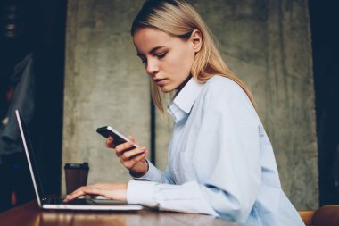 Dalgın genç kadın serbest meslek smartphone aygıt üzerinde gelen bildirim sırasında mesafesi iş modern dizüstü bilgisayar, okuma bağlı kablosuz 4 g için alanı coworking oturan internet