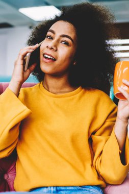 Yarım uzunluk portre sevimli neşeli kadın smartphone uygulama kapalı oturan üzerinden arkadaşlarınızla iletişim. Ofiste cep konuşurken kameraya bakarak mutlu kadın kişi