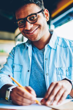 Yarım uzunluk portre yakışıklı gülümseyen erkek Tasarımcısı'nda kağıda yeni çizimler oluşturma şık gözlük. Projelendirme yeni başlangıç kapalı otururken kameraya bakarak başarılı iş adamı