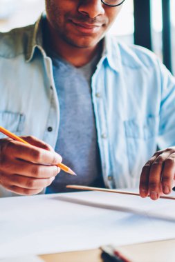 Kırpılmış görüntü akıllı yaratıcı erkek mimar planları üzerinde kapalı oturma sırasında çalışma trendy kot elbise giymiş. Kalem ve kural skeçler oluşturulurken holding adam eller odaklanmak