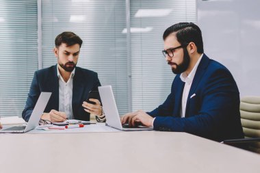 Dalgın iki profesyonel finans şirketi patronla tablo toplantıda çalışma brifing sırasında dizüstü bilgisayarlarda bilgi aramak. Gurur CEO'su posta smartphone meslektaşları ile işbirliği üzerinde kontrol