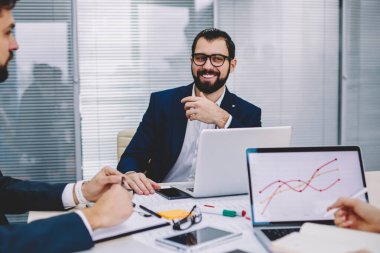 Formal Giyim tablo office iç netbook'lar ile Toplantı oturan iş meslektaşları ile tartışma sırasında ortaklık ayrıntılarını gülüyor pozitif profesyonel erkek girişimci giymiş