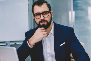 Formal giyim süre mali rapor yazma ve kurumsal şirket ofisinde oturan modern dizüstü bilgisayarda çalışan kameraya bakarak yarım uzunluk portre başarılı gurur CEO giymiş