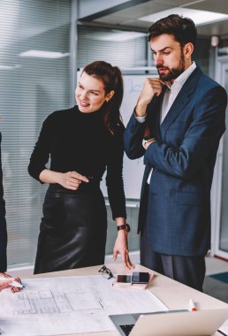 Ofisinde oturum beyin fırtınası sırasında meslektaşları için iyi fikirler açıklayan genç akıllı profesyonel erkek mimar. Deneyimli çalışan grubu formal giyim birlikte işbirliği içinde giyinmiş