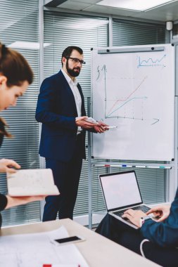 Flip grafik yanında duran ve dizüstü bilgisayar boş kopya alanı ekran reklam bilgin ile içerik tutan meslektaşları için açıklayan gözlük içinde icra müdürü deneyimli