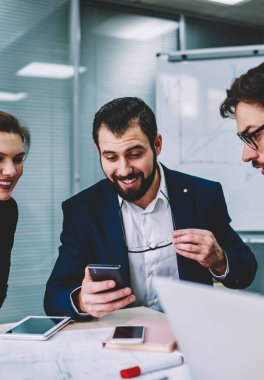 Genç yetenekli gülümseyen iş arkadaşlarınızla birlikte smartphone cep telefonu ile Web sitesi komik video izlerken iyi internet'e bağlı. Grup çalışma molası sırasında eğlenmek akıllı duygusal Mimarlar