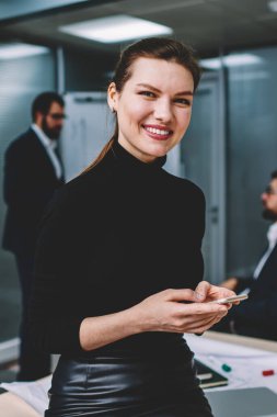 Güzel başarılı akıllı kadın yönetici modern smartphone komik iletiler gönderilirken gülümseyen yarım uzunluk portre. Büyüleyici neşeli işkadını kapalı kameraya bakarken gülüyor