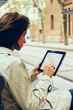 Genç kadın sahte alanı Web sitesi içerik tramvay durağı üzerinde oturan için modern Dokunmatik ped cihaz üzerindeki metin yazarak. Hipster blogger tablet ile boş perde reklam için web sayfasında bir haber okuma