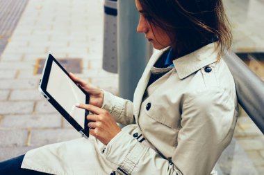 Parmak sahte uygulama açık havada tramvay durağı üzerinde oturan 4 g internet bağlantısı üzerinden yüklemelerde seçme modern Dokunmatik ped cihaz ekranı ile dokunmadan dalgın kadın hipster blogger yan görünüm