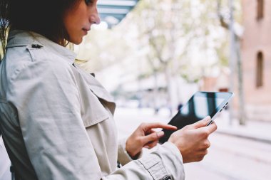 Modern Dokunmatik ped cihaz ücretsiz 4 g internet bağlantısı üzerinden indirmek için uygulama seçimi rahat giyinmiş hippi kız yan görünüm. Genç kadın tramvay durağı kentsel ortamda ayakta e-kitap okuma