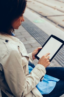 Şık giyimli genç kadın sahte ekranı modern dokunmatik yüzey üzerinde parmak ile dokunmadan yan görünüm bağlı 4 g için taşıma tramvay durağı üzerinde oturup beklerken online alışveriş yaparken Internet