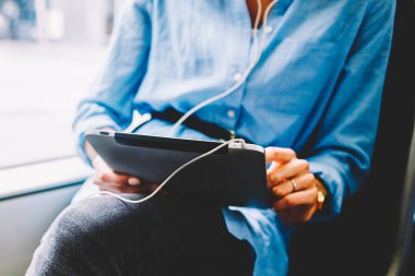 Dokunmatik yüzey üzerinde sosyal ağlar sohbet ve kulaklık bağlı tramvayda oturan aygıt radyo dinleme kadın yolcu görünümünü kırpılmış. 4 g kullanarak dijital tablet holding kadının eller Internet