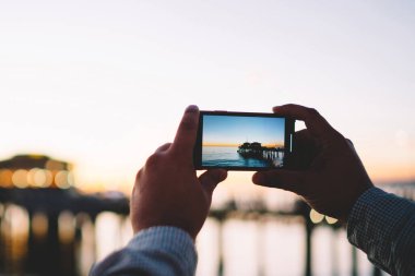 Akşamları güzel bir çevre ve denizin görüntüsünü çizen erkek cep telefonunda iyi bir uygulama, alacakaranlıkta okyanusun görüntüsünü çeken erkek, modern akıllı telefon ve kamera ile karanlıkta fotoğraf çekiyor.