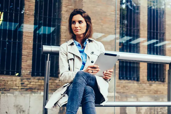 Düşünceli şık hippi kız tramvaya bekleyen tarafında ararken ücretsiz 4 g internet bağlantısı ile modern dokunmatik yüzey üzerinde uygulama yükleme. Otobüs durağı üzerinde oturan tablet ile genç kadın durulması