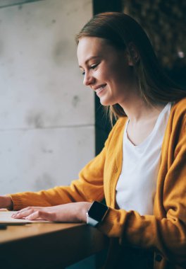 Sosyal ağlarda eğlenceli videolar izleyen neşeli bir kadın dizüstü bilgisayarda multimedya uygulaması kullanıyor, genç hippi kız netbook 'ta yazı yazmaktan heyecanlanıyor ve kapalı alandaki işin tadını çıkarıyor.