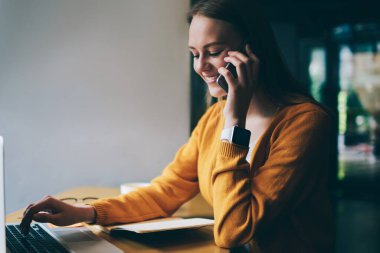 Kafeteryadaki kablosuz 4G bağlantısını kullanarak modern dizüstü bilgisayarda mesaj yazarken akıllı telefon cihazıyla arkadaşınla iletişim kuran sevimli yüzlü pozitif kadın serbest çalışan.